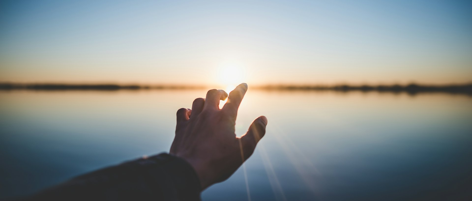 Hand vor der Sonne über dem Wasser